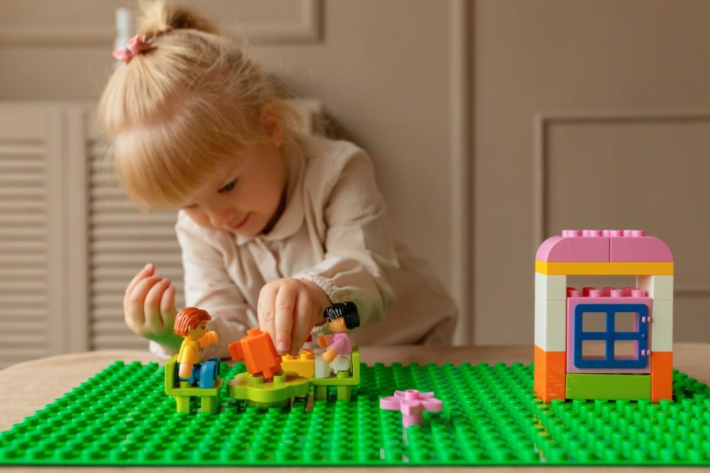 A young girl engaging creatively with colorful plastic building blocks on a table indoors.
