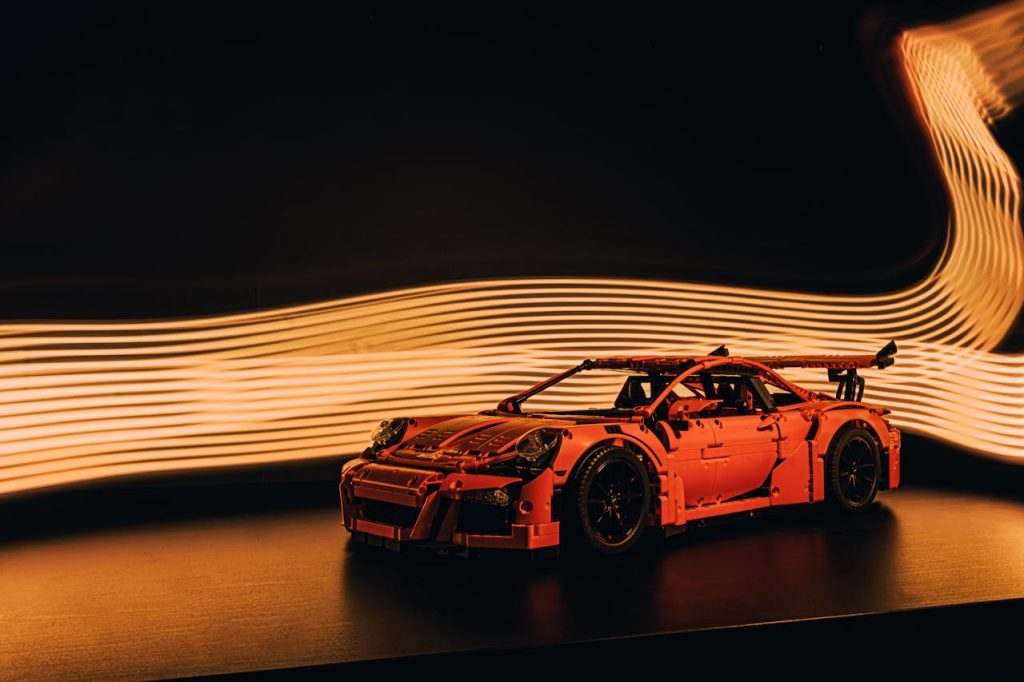 Red toy sports car in motion with dynamic light painting effect against dark background.