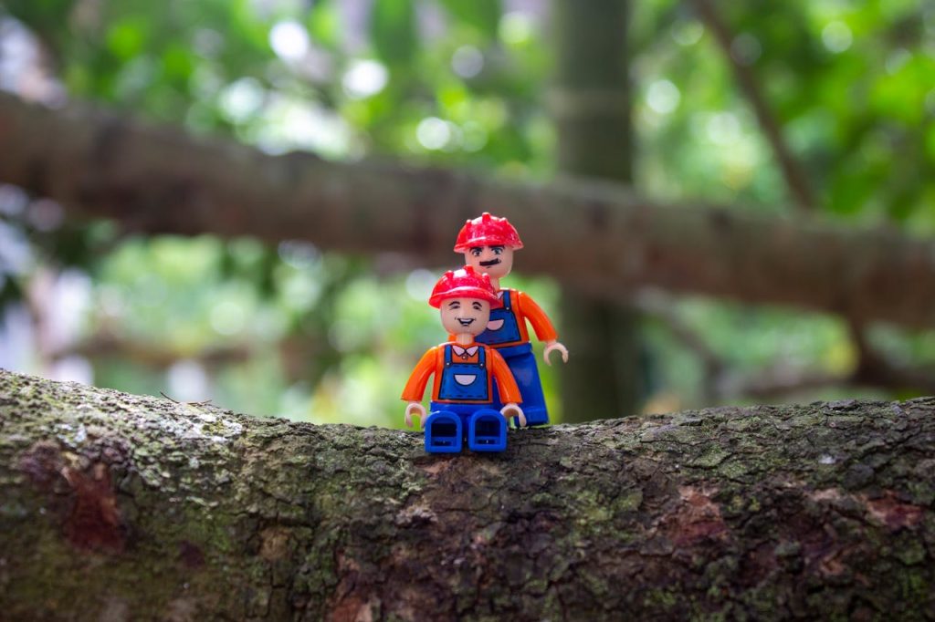 Two toy figurines on a tree branch amidst a natural green background.